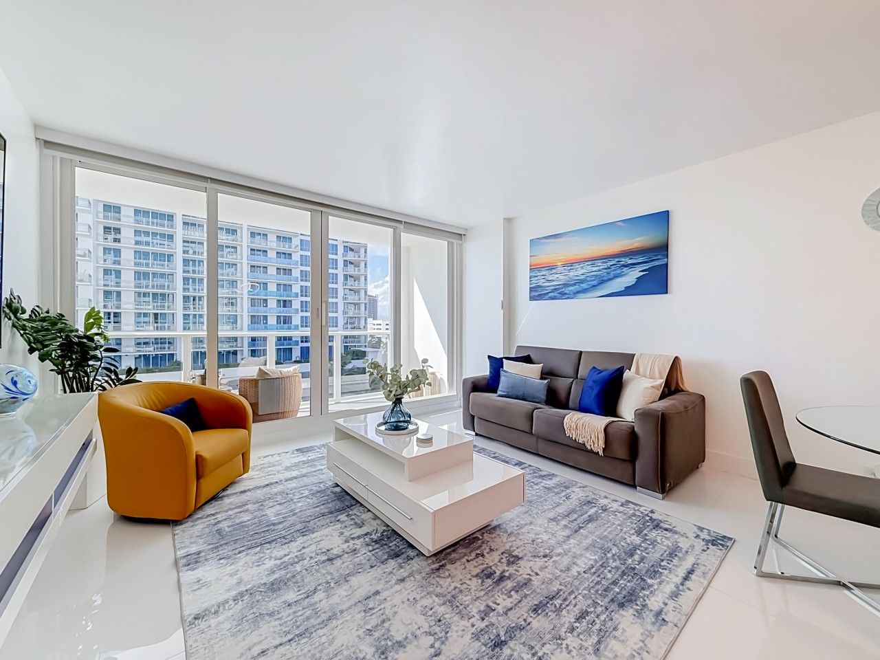 A modern living room with a sofa, coffee table, and a view of a cityscape through large windows.