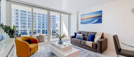 A modern living room with a sofa, coffee table, and a view of a cityscape through large windows.