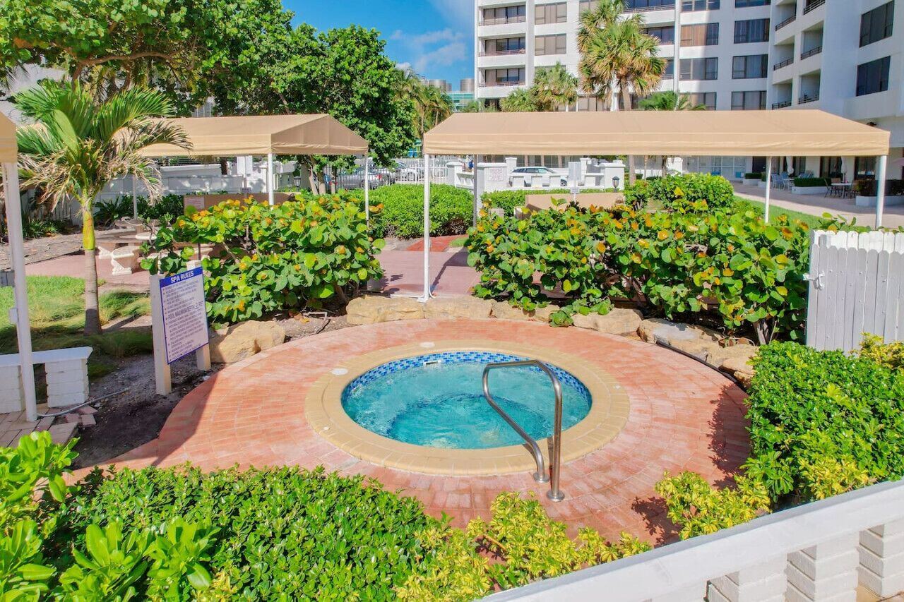 A pool area with a circular hot tub, surrounded by lush greenery and covered seating areas.