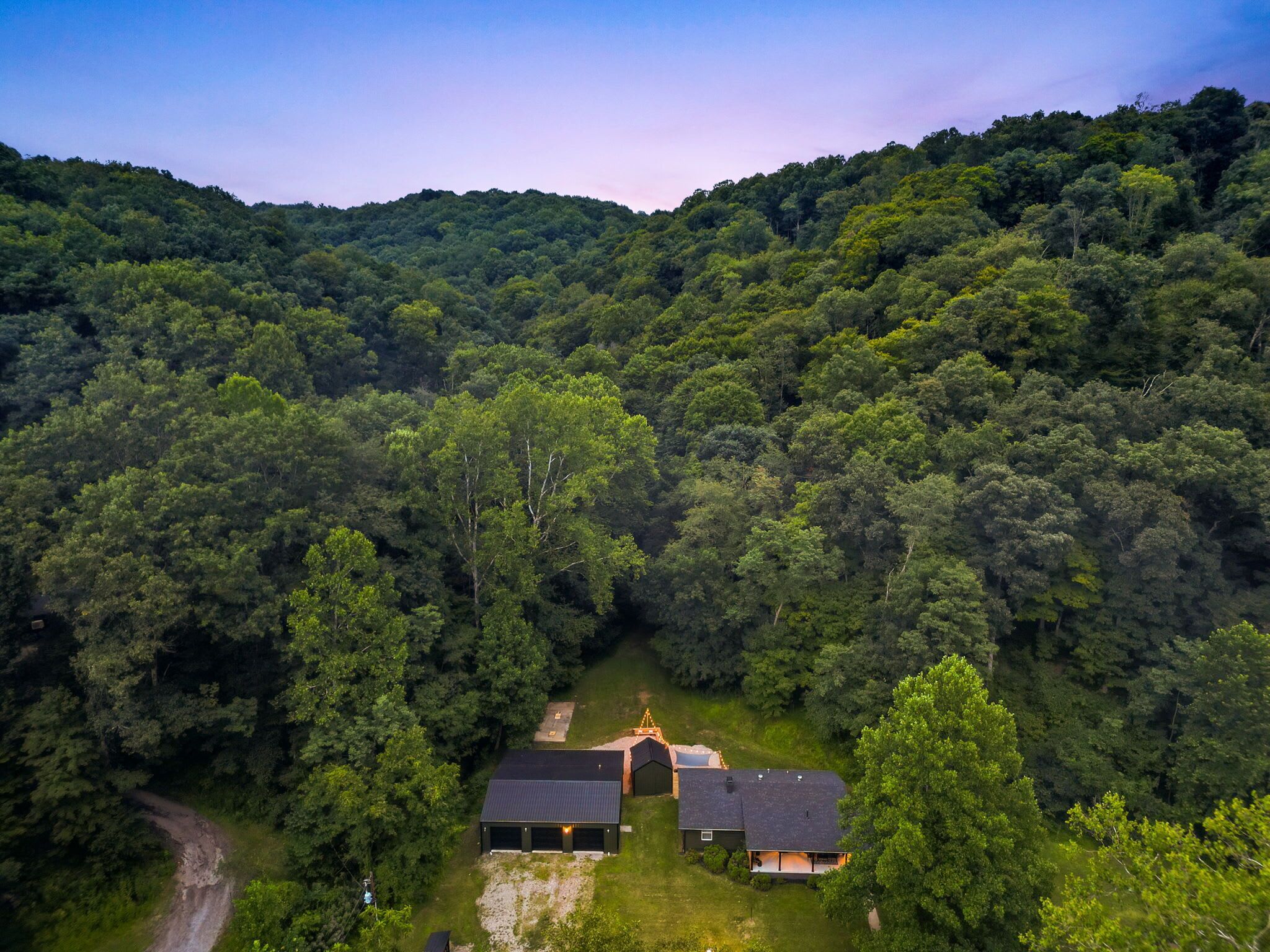 Une propriété rurale comprenant une grande maison, une grange et une allée menant à la forêt.