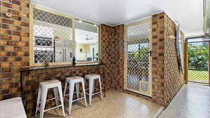 Un baño con pared de ladrillo, un espejo grande y tres taburetes blancos.