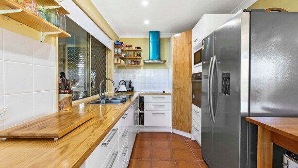 Una cocina moderna con refrigerador de acero inoxidable, encimeras de madera, gabinetes blancos y salpicadero de azulejos.