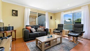 Una sala de estar con un sofá, dos sillones, una mesa de centro y un mueble de televisión con dispositivos electrónicos.
