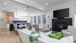 A modern living room with a fireplace, a television, and a dining area with a kitchen in the background.