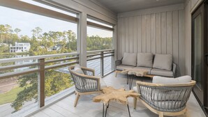 A balcony with a view of a lake, a sofa, two chairs, and a wooden coffee table.