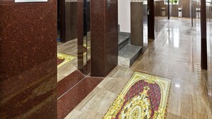 Un hall d’hôtel moderne avec un sol en marbre, une moquette à motifs et un plafond orné de lambris en bois.