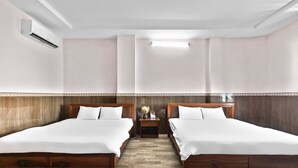 Une chambre d’hôtel avec deux lits, des têtes de lit en bois, une petite table de chevet avec un vase, et un grand miroir au mur.