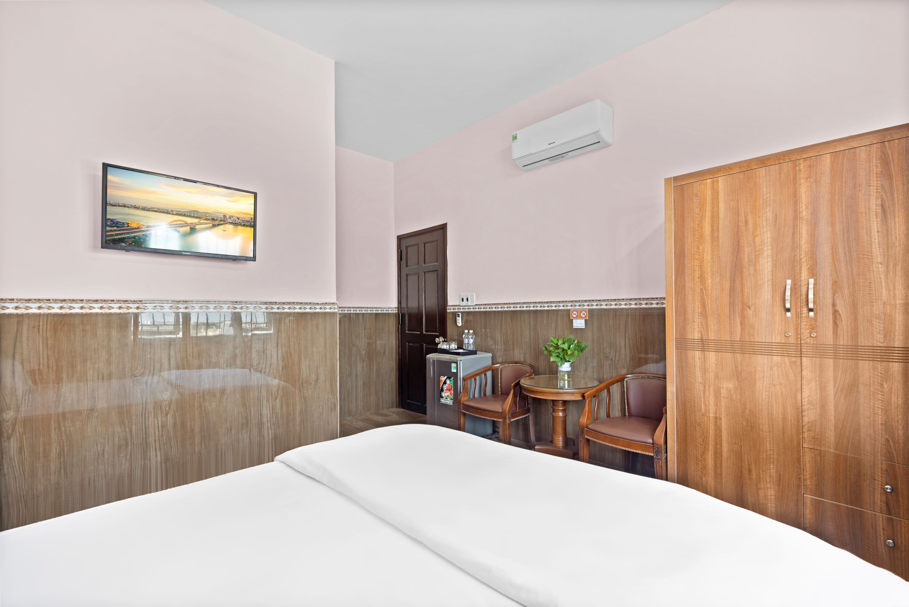 Habitació d'hotel amb un llit, una taula petita amb cadires, un armari de fusta, aire condicionat fixat a la paret, un quadre i una porta.