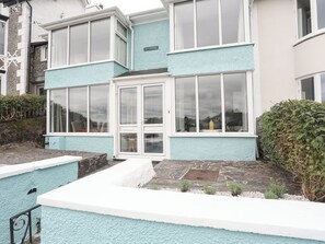 A two-story house with a light blue exterior, a white door, and a small garden area with a stone pathway. - Ivy Cottage (Porthmadog)
