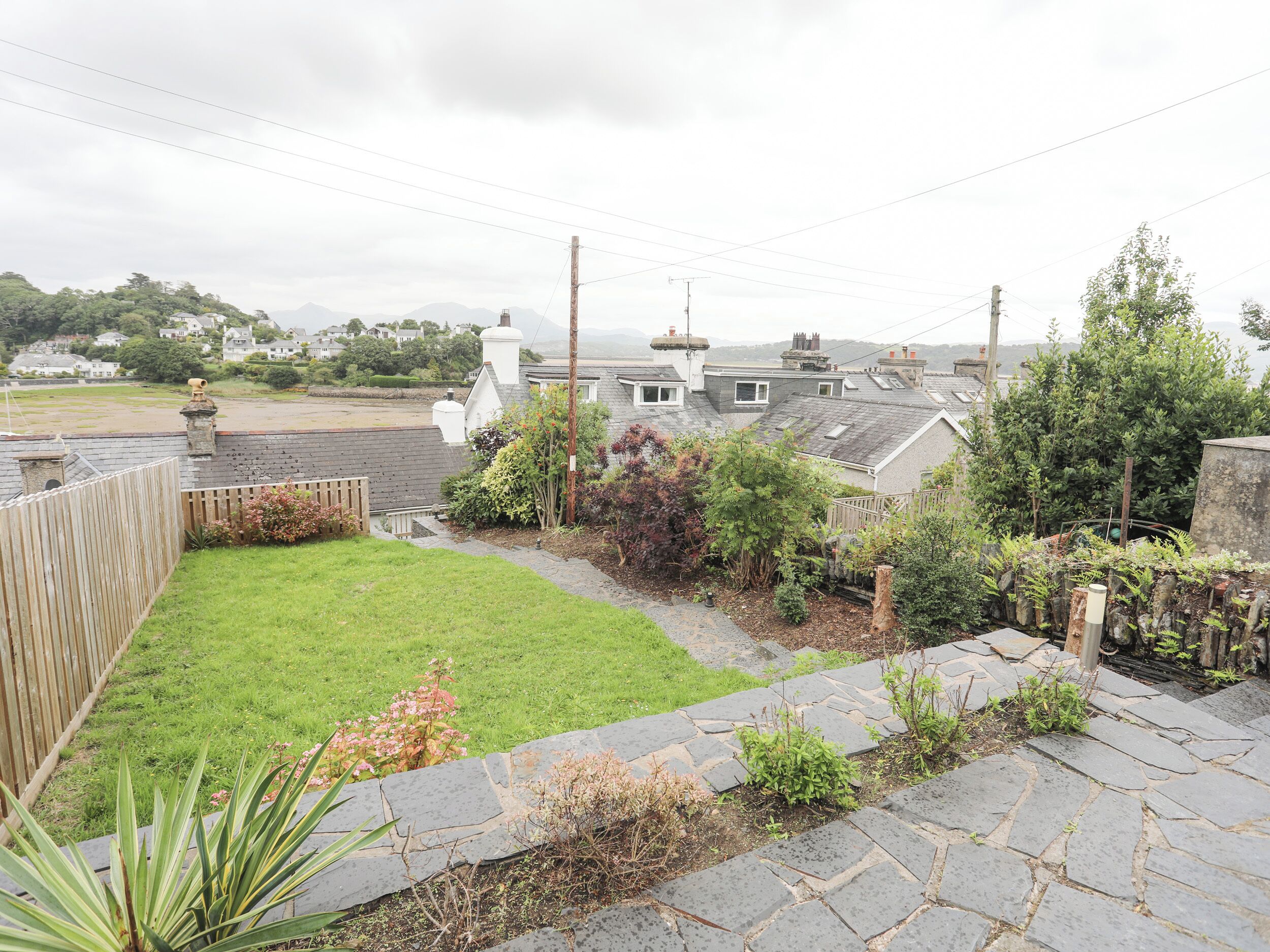 A residential area with a grassy backyard, stone pathway, and a view of houses and hills in the distance.