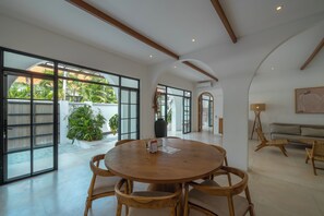 Une pièce spacieuse avec une table ronde en bois et des chaises, de grandes fenêtres et une vue sur la verdure environnante.