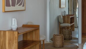 A modern interior with a wooden desk, a chair, a white vase, and a large abstract painting. - Villa Eliad - 3 Bedroom Villa in Berawa (Canggu)
