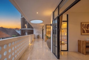 Un pasillo con una puerta de cristal que da a una habitación, una planta en maceta y vistas al cielo.
