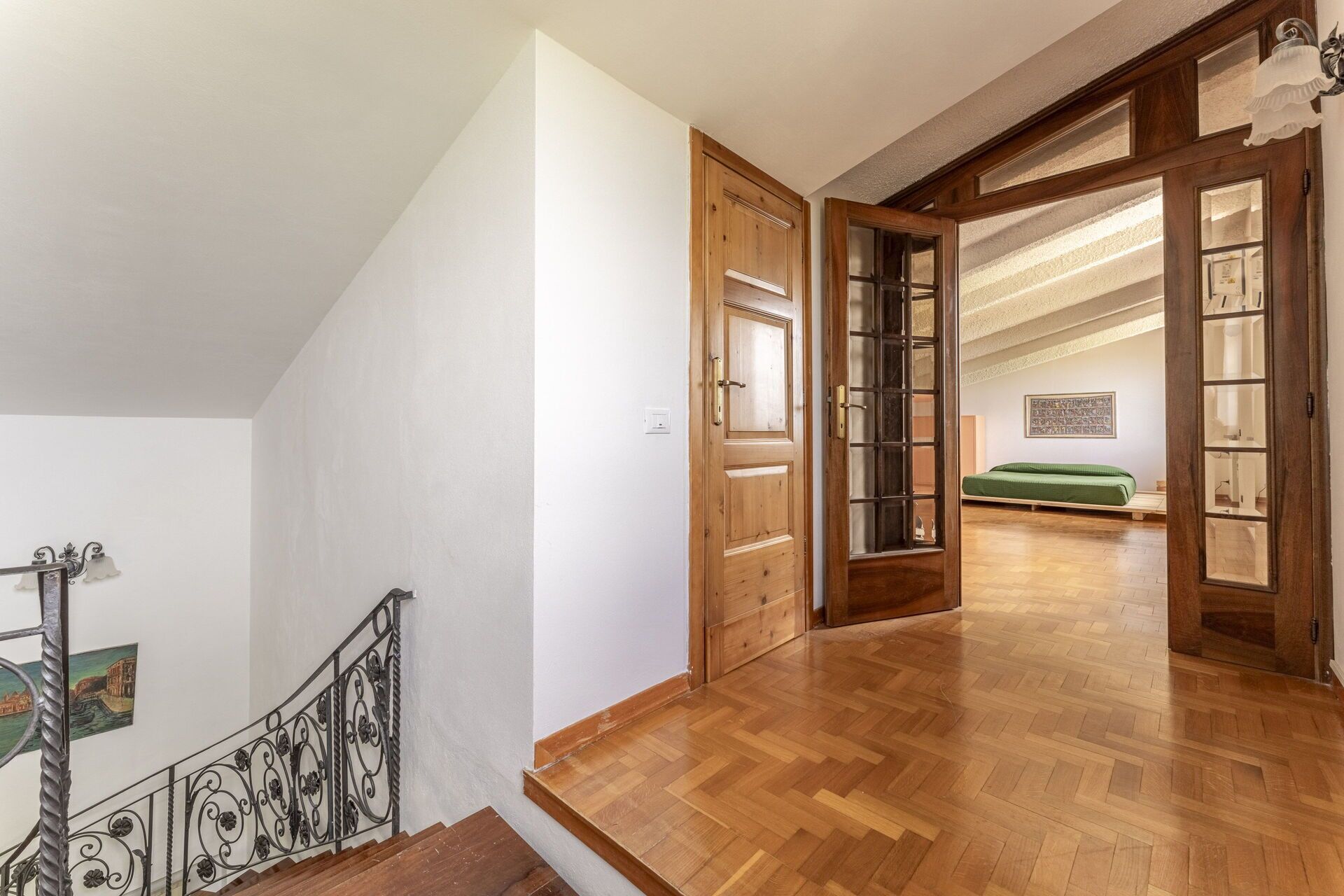 A wooden staircase leading to a room with a green bed and a wall-mounted shelf.