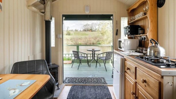 A cozy kitchen with a dining area, a stove, and a view of the outdoors. - Cosy, peaceful & secluded lakeside cabin. BBQ, Firepit, Fishing, Dogs welcome. (Hadlow Down)