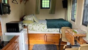A compact room with a bed, a small kitchenette, a wooden desk, and a chair. - Snug secluded lakeside shepherds hut for fishing, or just relaxing.  (Hadlow Down)