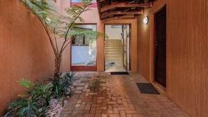 A narrow brick pathway leading to a wooden door with a glass panel, surrounded by plants and a textured wall. - San Lameer Villa 14323 (Southbroom)