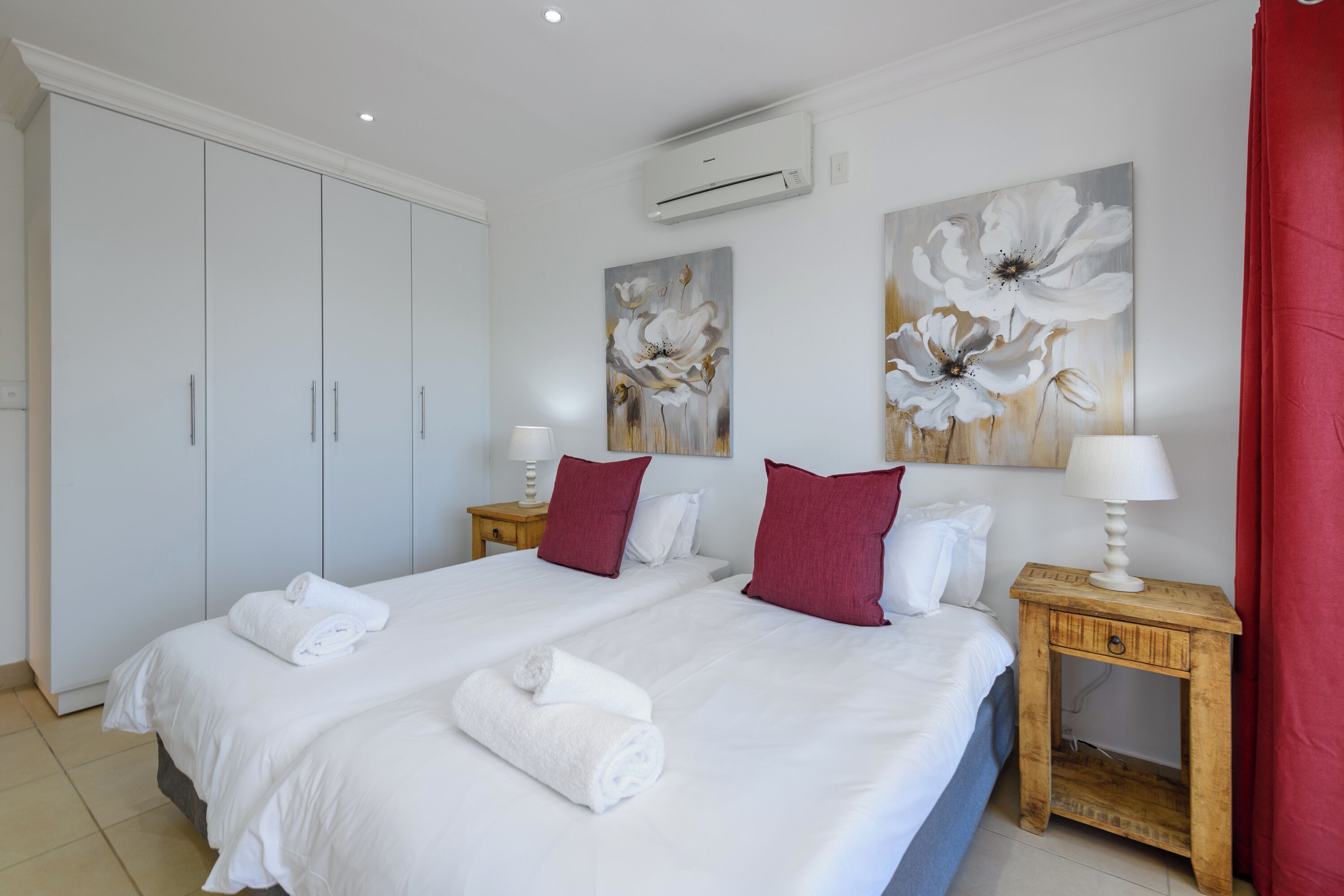A hotel room with a large bed, two nightstands, a wardrobe, and floral artwork on the walls.