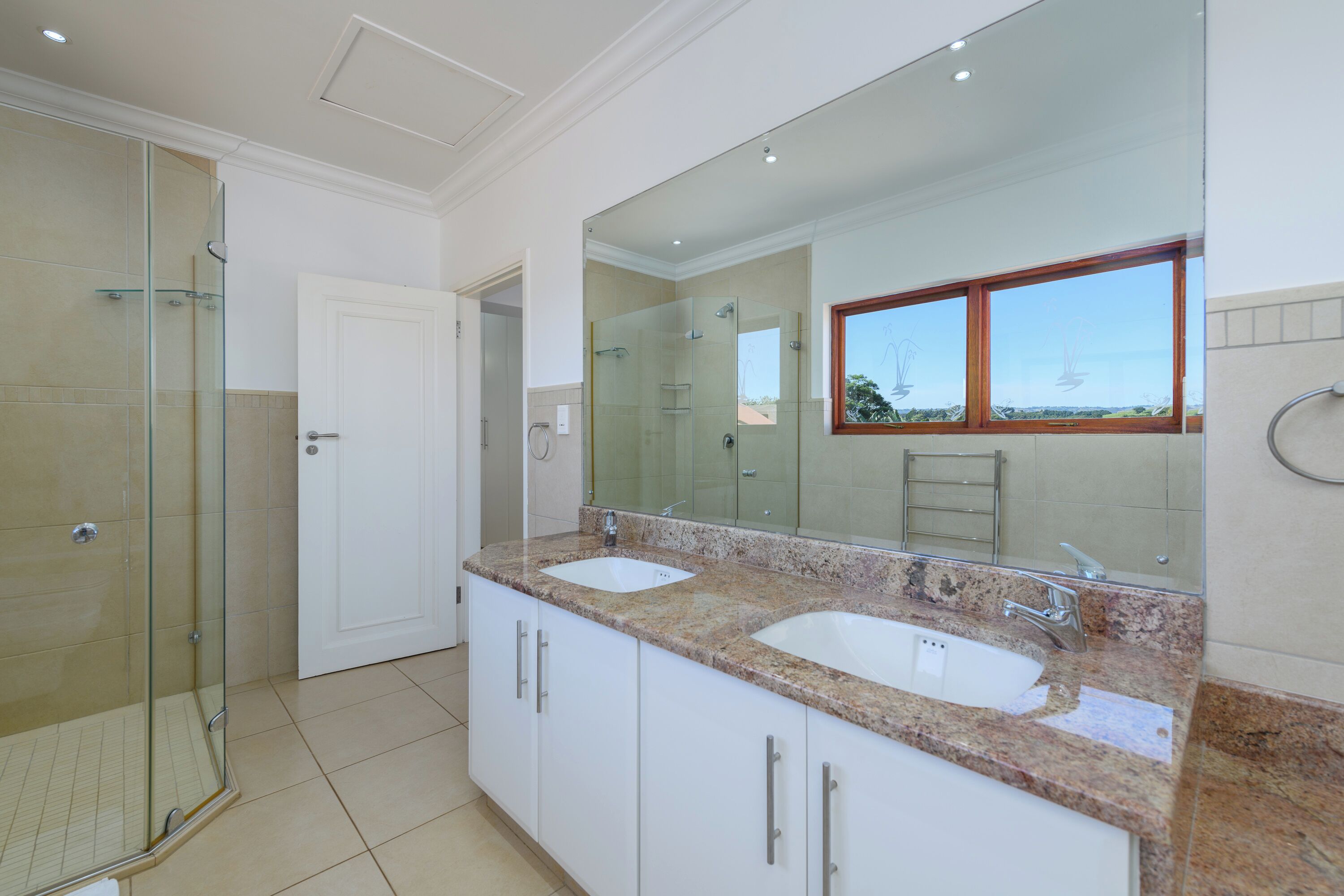 A bathroom with two sinks, a large mirror, and a glass shower enclosure.