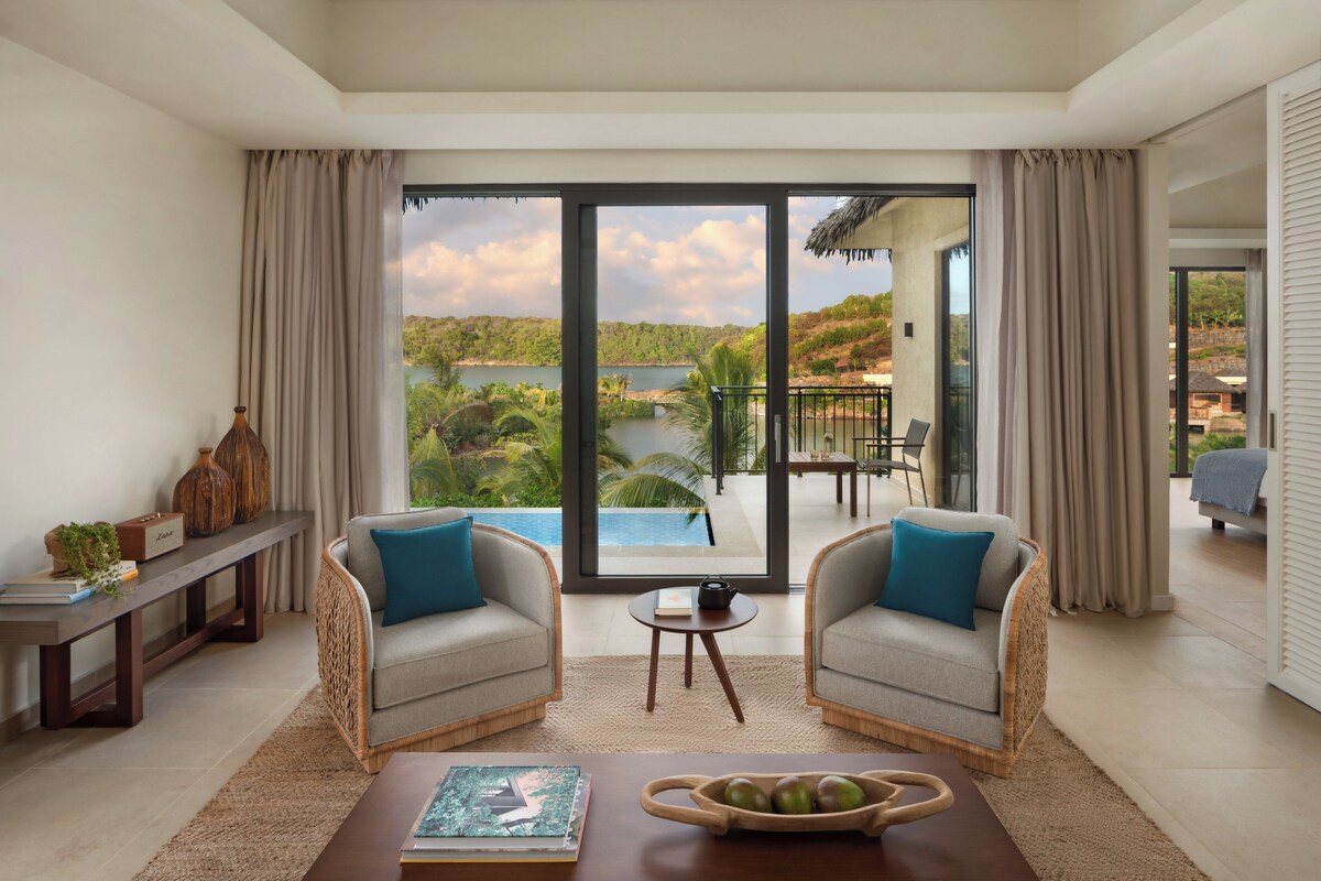 A spacious living room with two sofas facing a large sliding glass door that opens to a scenic outdoor area with a pool and lush greenery.