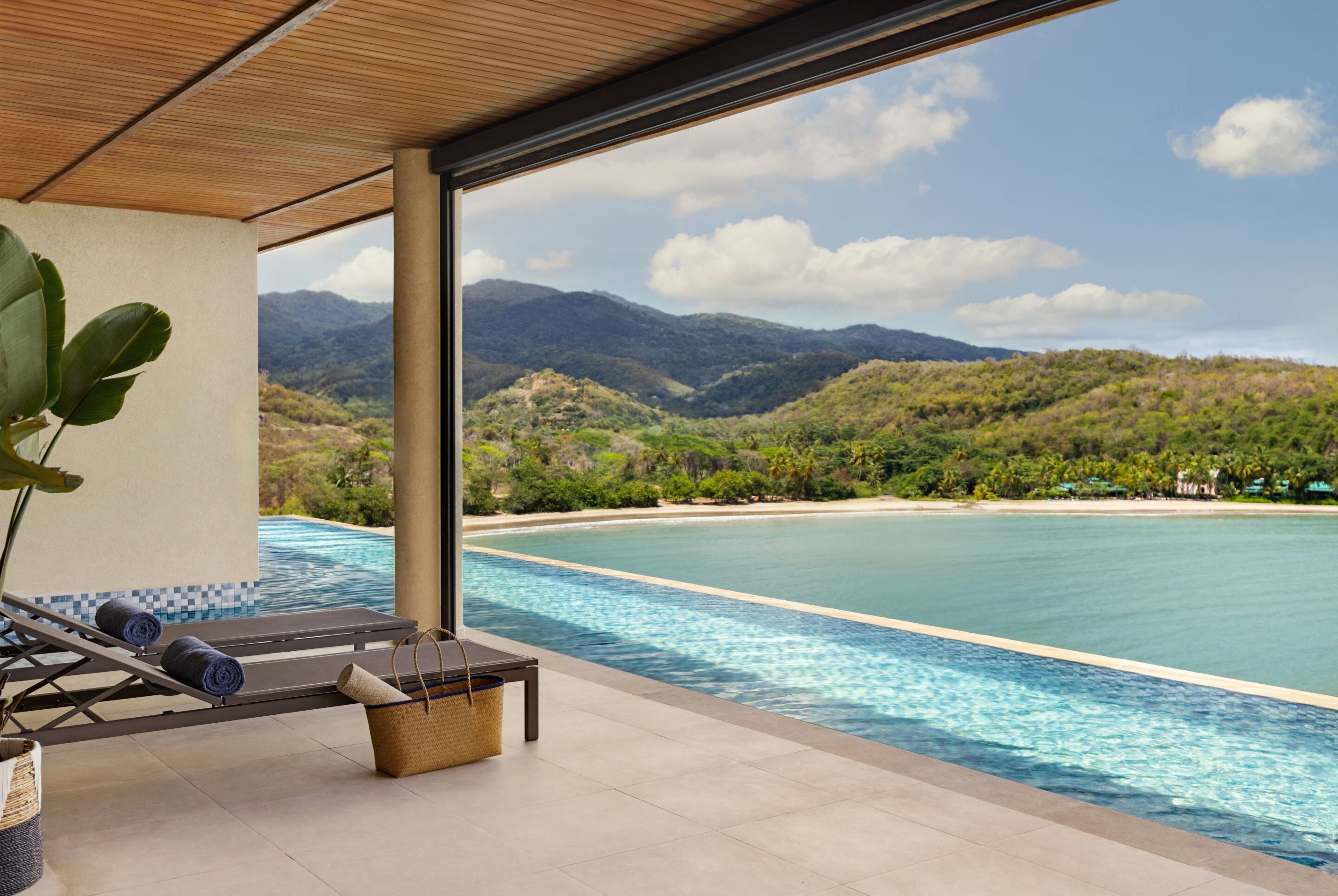 A poolside area with lounge chairs and a view of a beach and mountains.