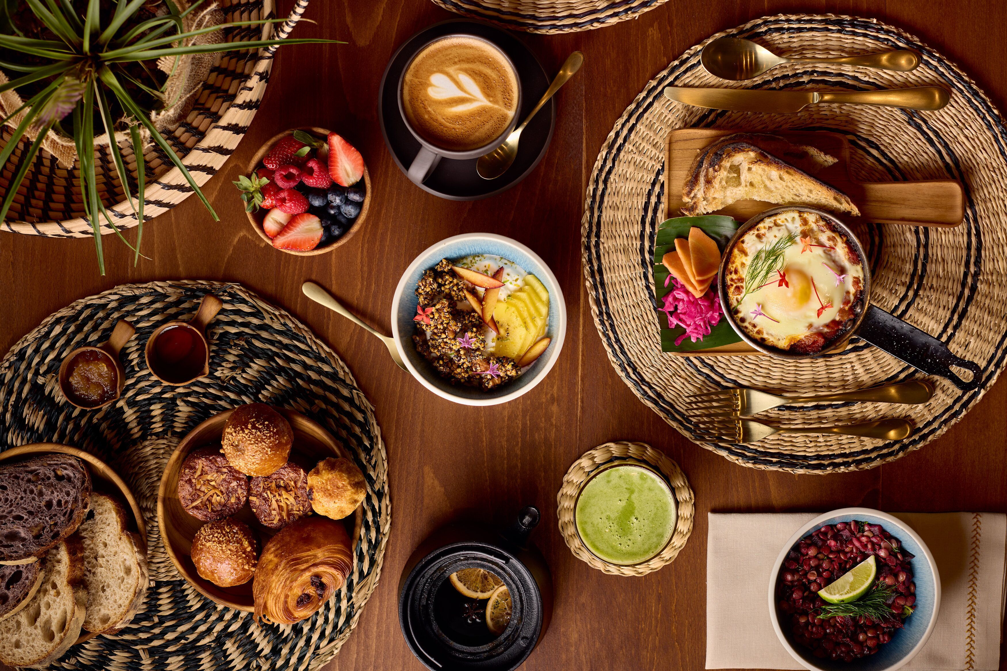 Una mesa de desayuno con diversas opciones de comida, incluyendo pan, pastelería y una taza de café.