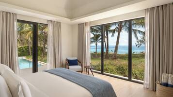 A bedroom with a large bed, a chair, a small table, and a view of a pool and ocean.