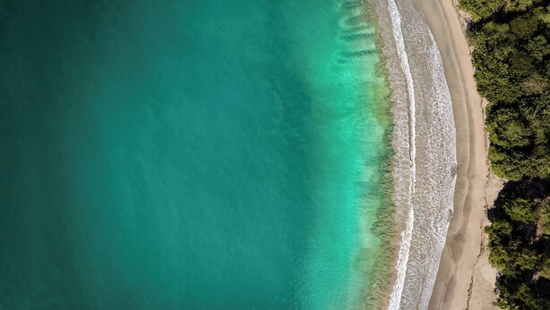 Vista aérea de una playa con aguas turquesas cristalinas y una orilla arenosa.