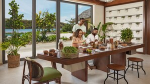 A modern kitchen with large windows overlooking a scenic view, a central island with stools, and a wall-mounted plant display. - Six Senses La Sagesse (St. David)