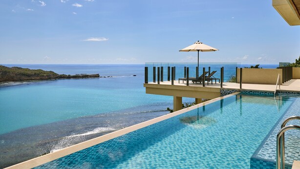 A clear blue pool with a view of the ocean, a lounge area with chairs and an umbrella, and a tiled deck. - Six Senses La Sagesse (St. David)