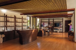 A spacious boutique hotel lobby with a wooden reception desk, shelves with various items, a clothing rack, and a large window allowing natural light. - Six Senses La Sagesse (St. David)