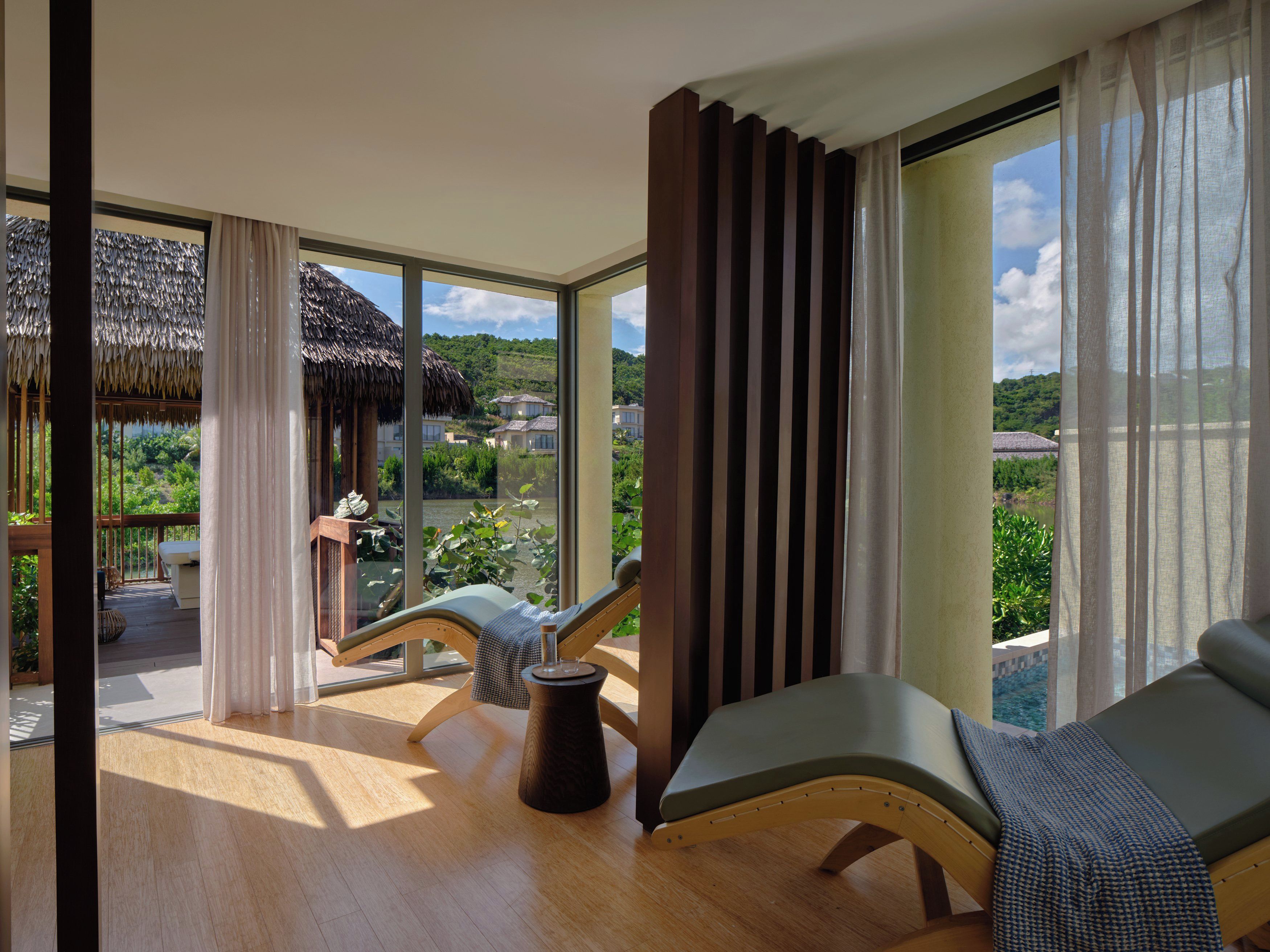 A room with a large window, a wooden floor, a chair, and a view of a landscape with houses.