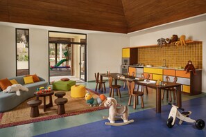A spacious living area with a sofa, coffee table, and play area. A kitchen with a dining table and chairs is visible. - Six Senses La Sagesse (St. David)