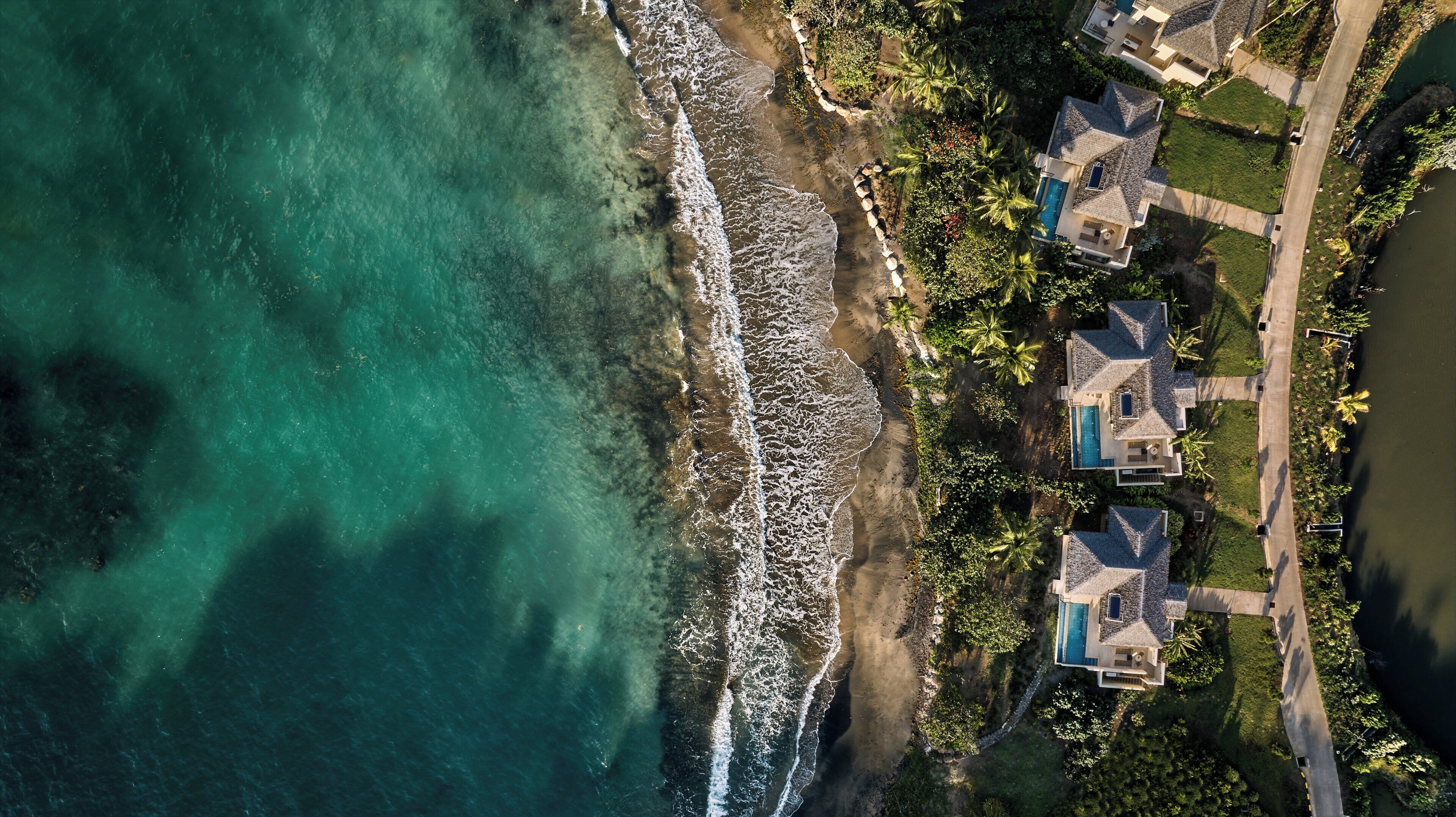 Vista aerea di una proprietà costiera con piscina, diverse case e spiaggia.