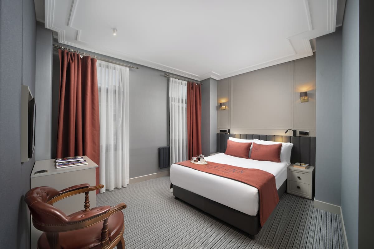 A hotel room with a large bed, a desk, a chair, and a TV.