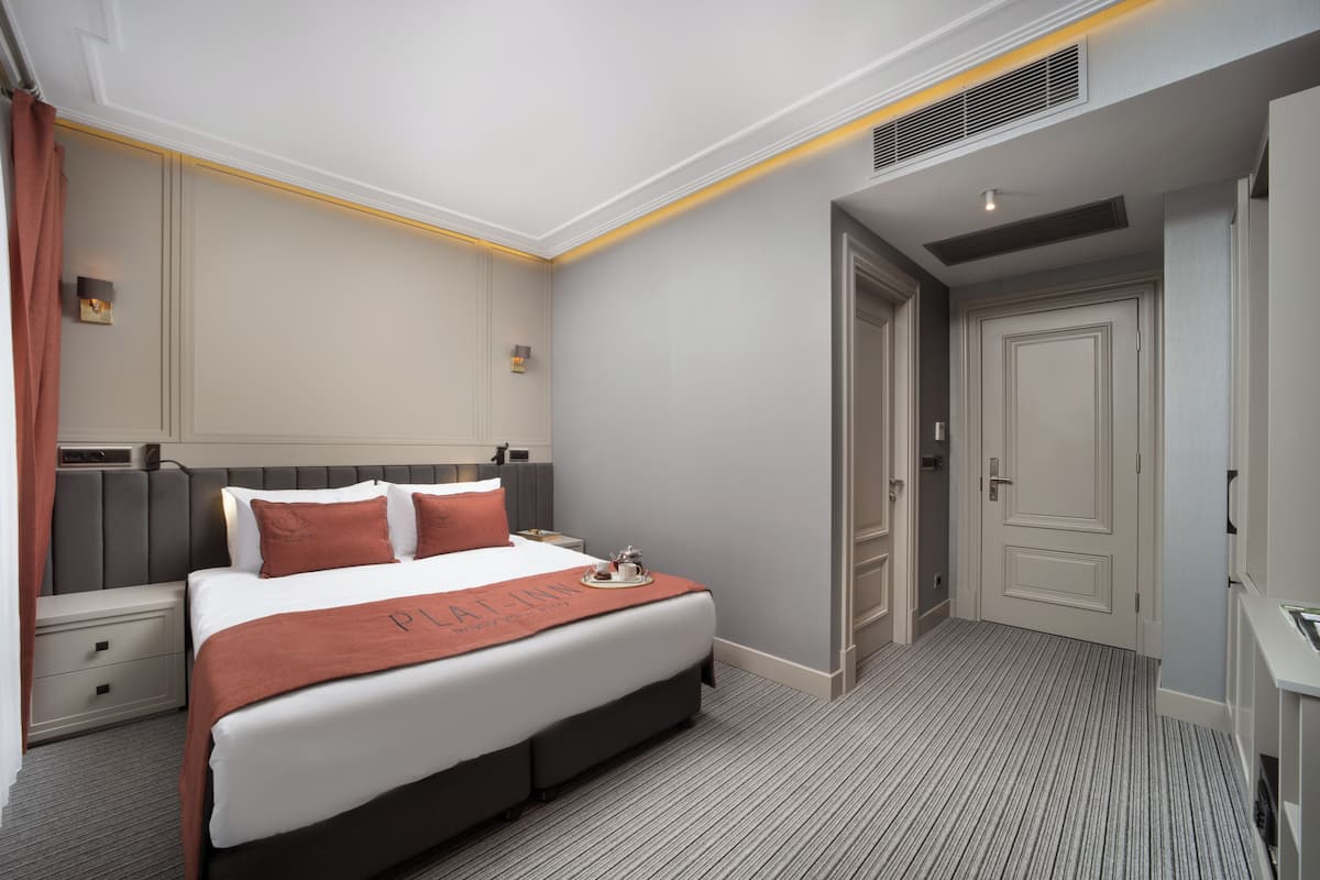 A hotel room with a large bed, a nightstand, a dresser, and a door.
