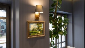En vägglampa, en inramad landskapsmålning och en krukväxt i en hall.
