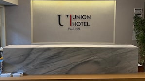 En receptionsdisk med en marmorskiva, en skylt med texten ”Union Hotel” och ”Plat Inn”, och en modern lampa ovanför.