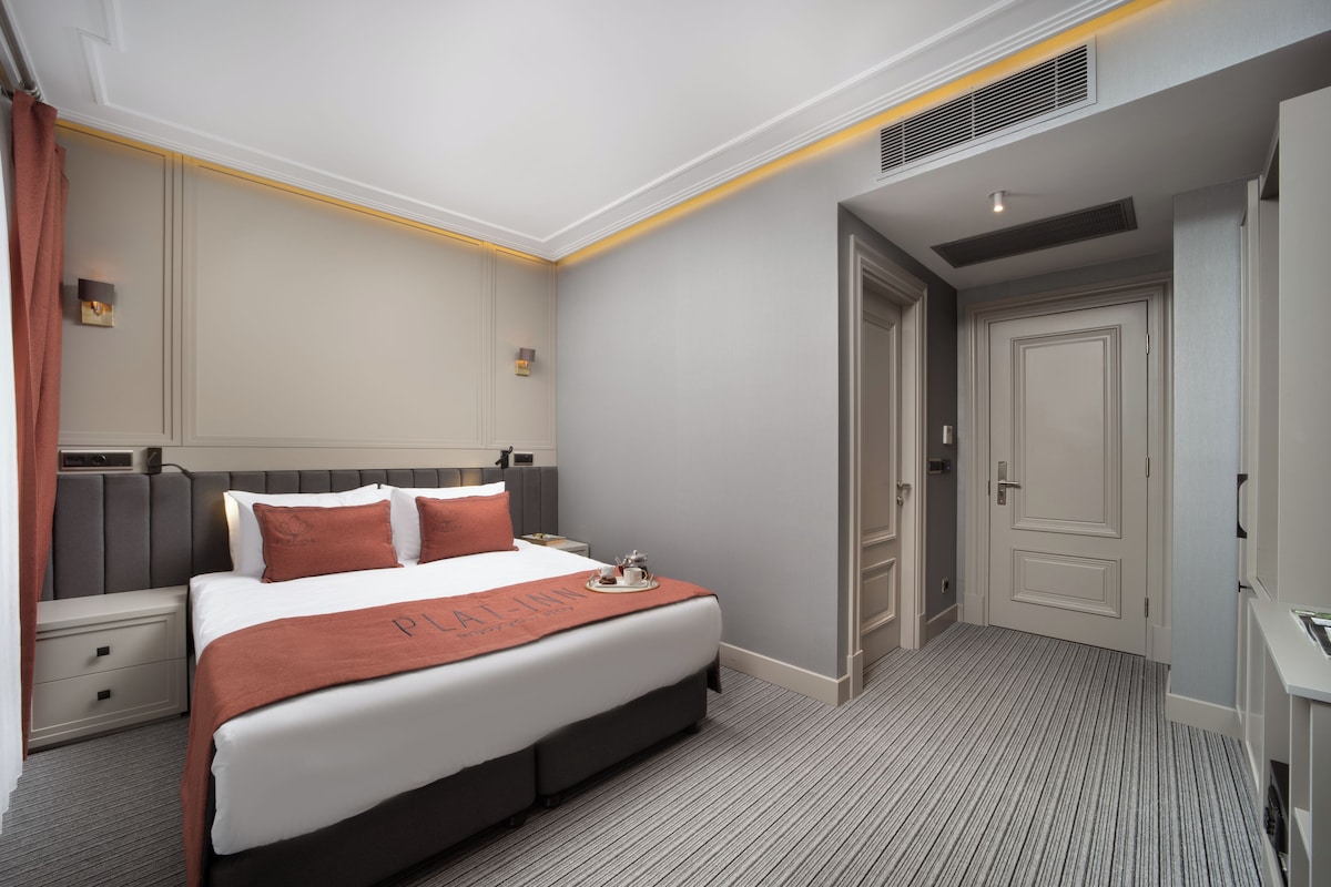 A hotel room with a large bed, a nightstand, a dresser, and a door.