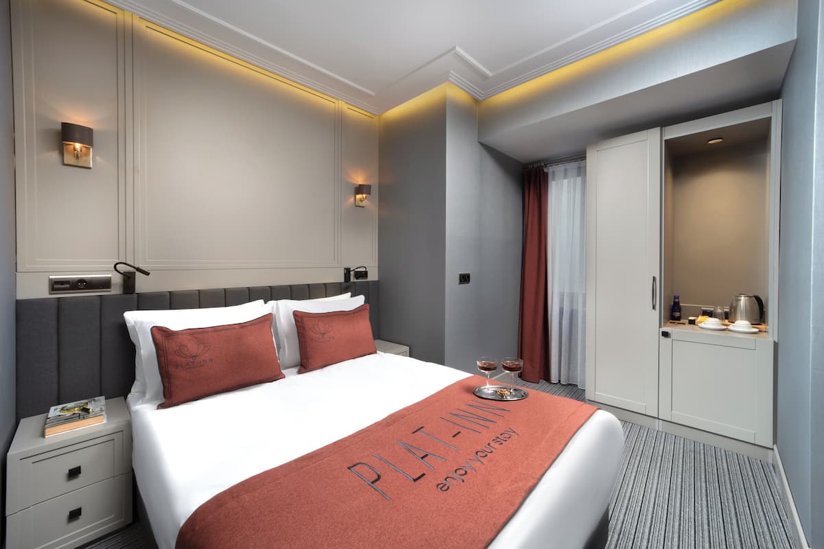 A hotel room with a large bed, a nightstand with a lamp, a wardrobe, and a tray with glasses and a bottle.