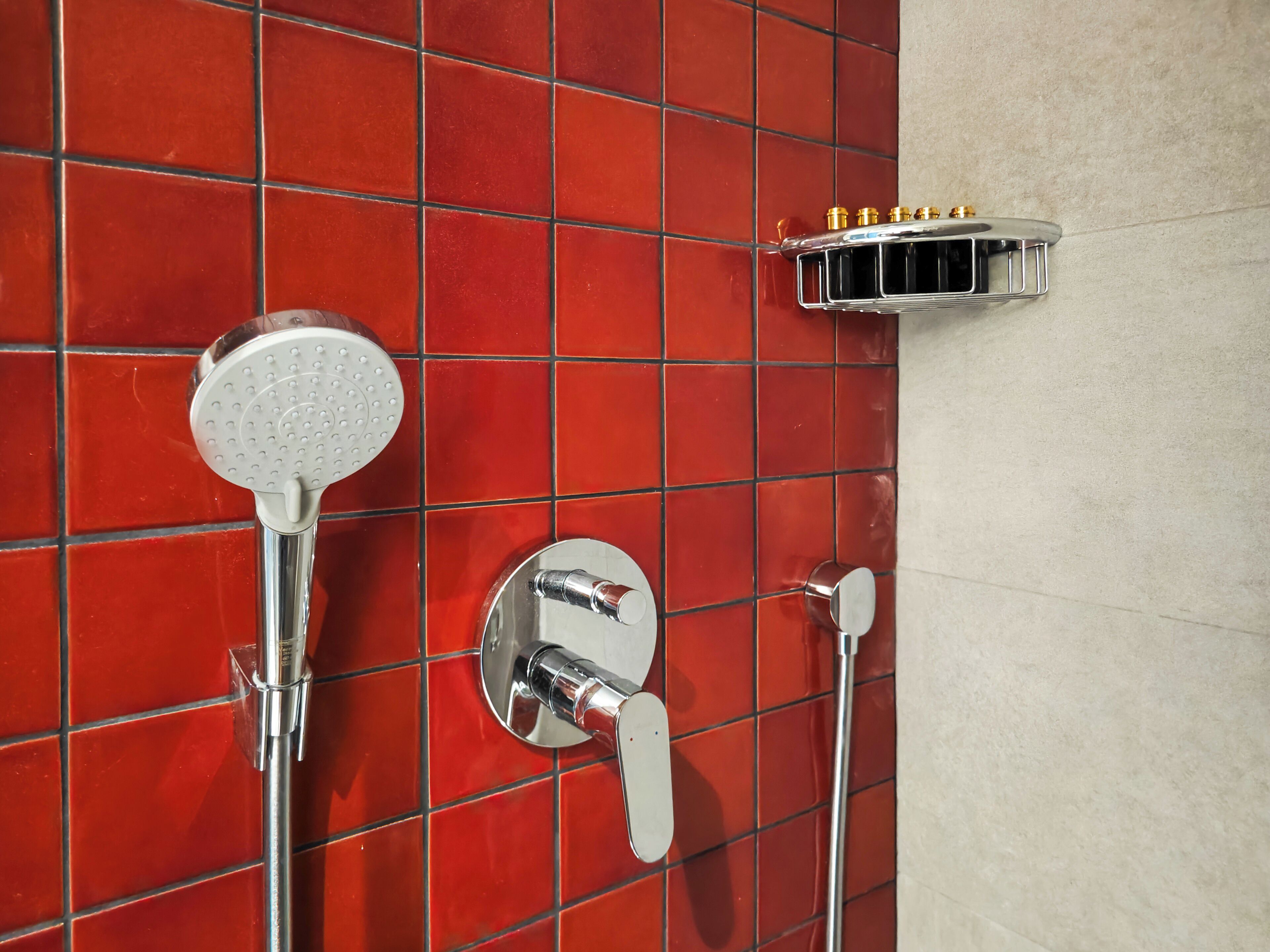 A bathroom with red tiled walls, a showerhead, and a chrome faucet.