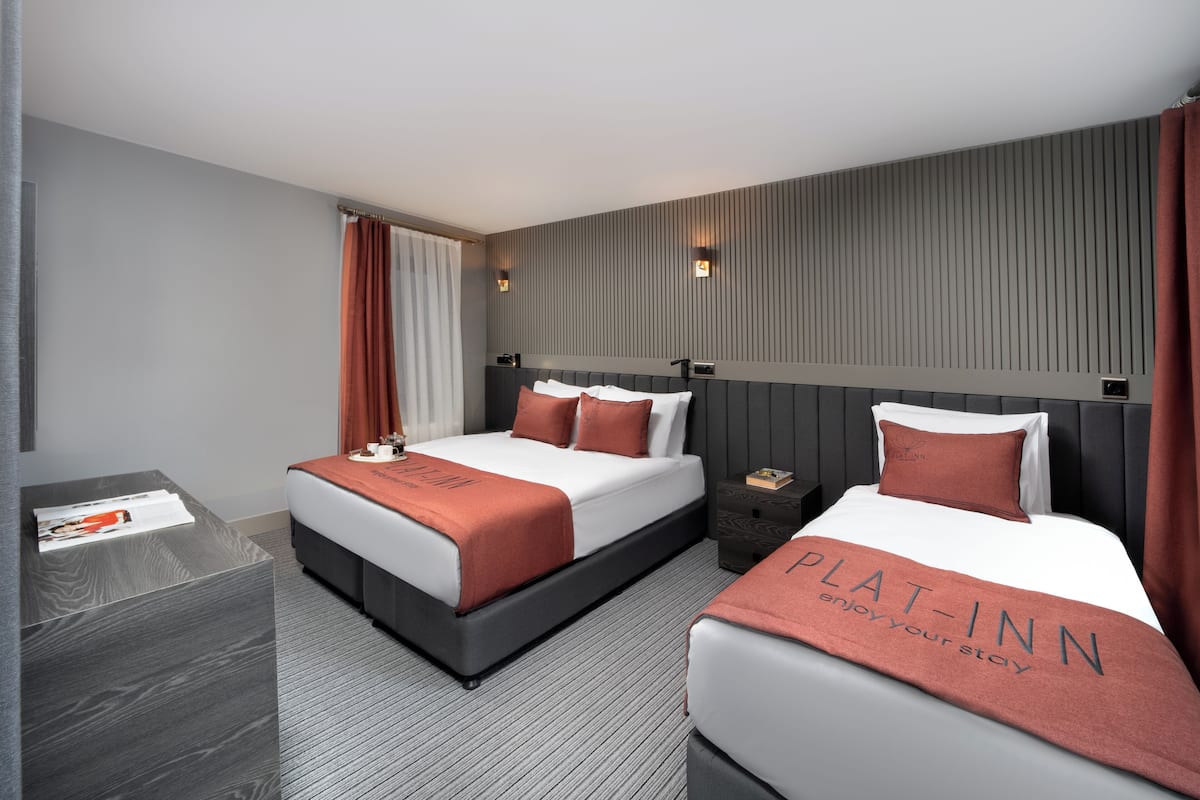 A hotel room with two beds, a nightstand, a small table, and a wall-mounted TV.