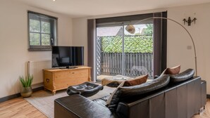 Una sala de estar moderna con un sofá de cuero, un mueble de madera, un televisor y un ventanal con vistas a zonas verdes.