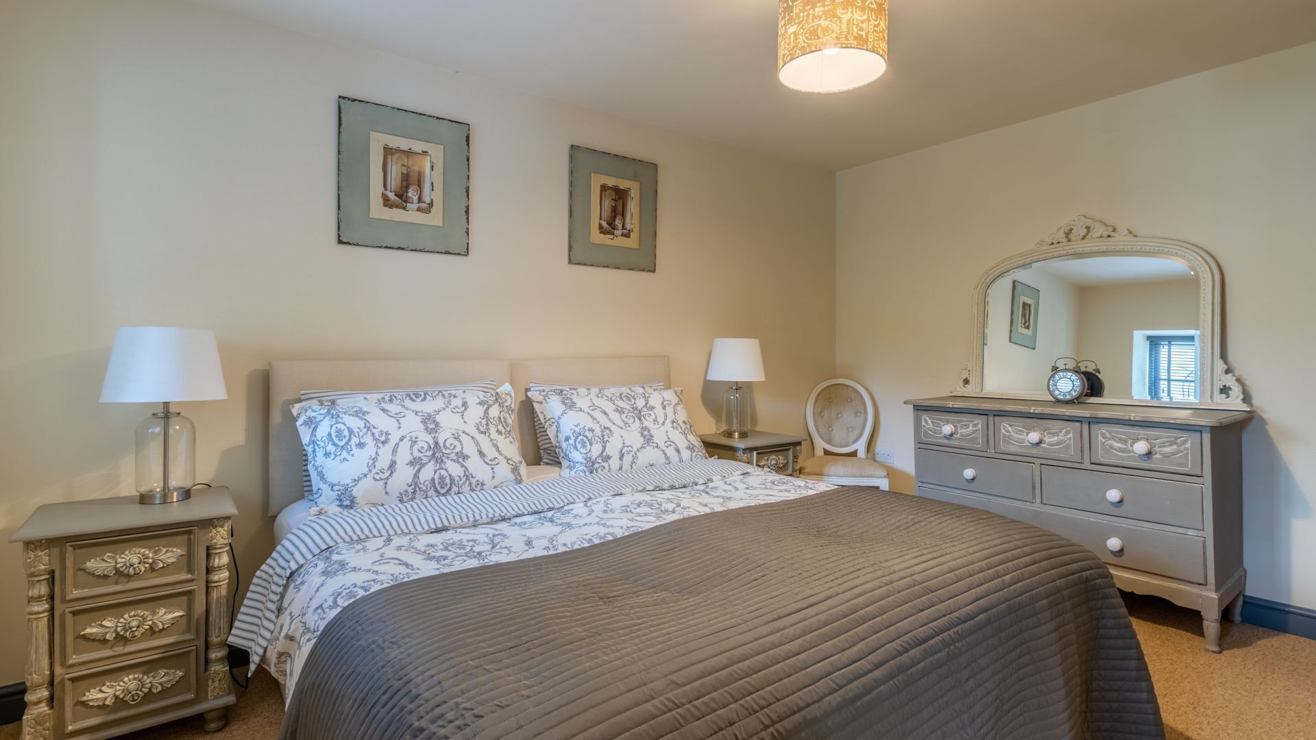 A bedroom with a bed, two bedside tables, a dresser, a mirror, and two wall-mounted pictures.