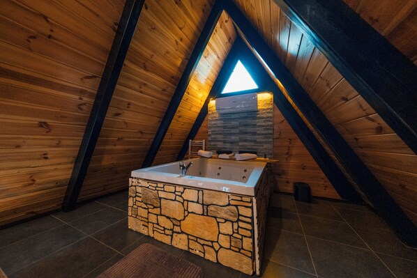 Una bañera de piedra en un dormitorio de ático con suelo de madera y tragaluz.