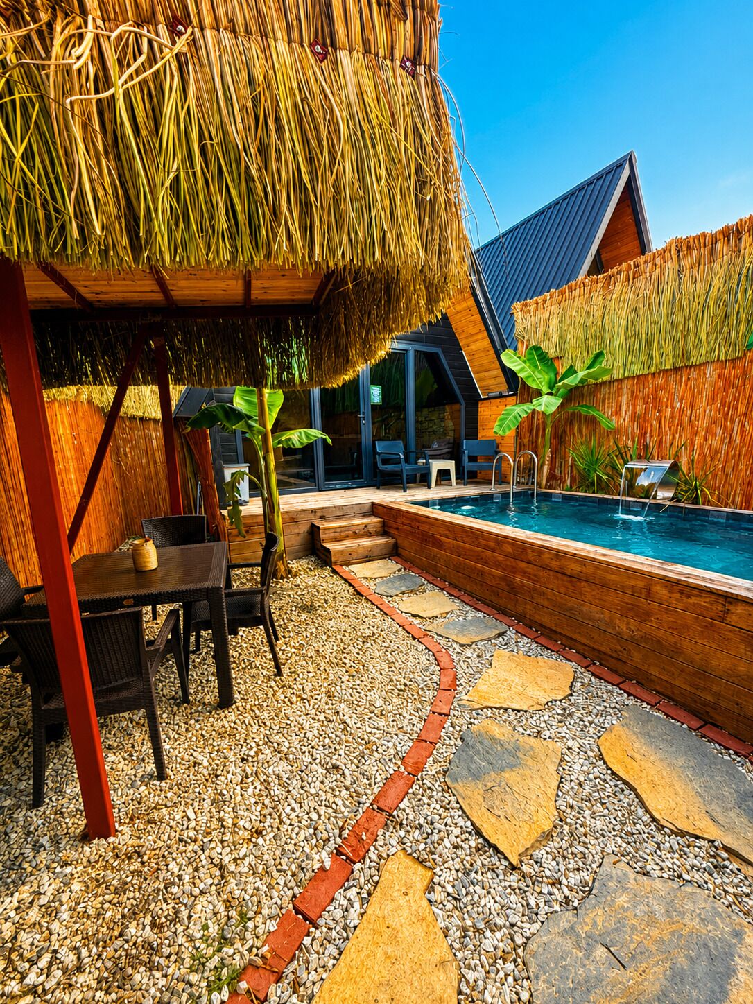 A pool area with a thatched roof structure, a stone pathway, and a wooden deck.