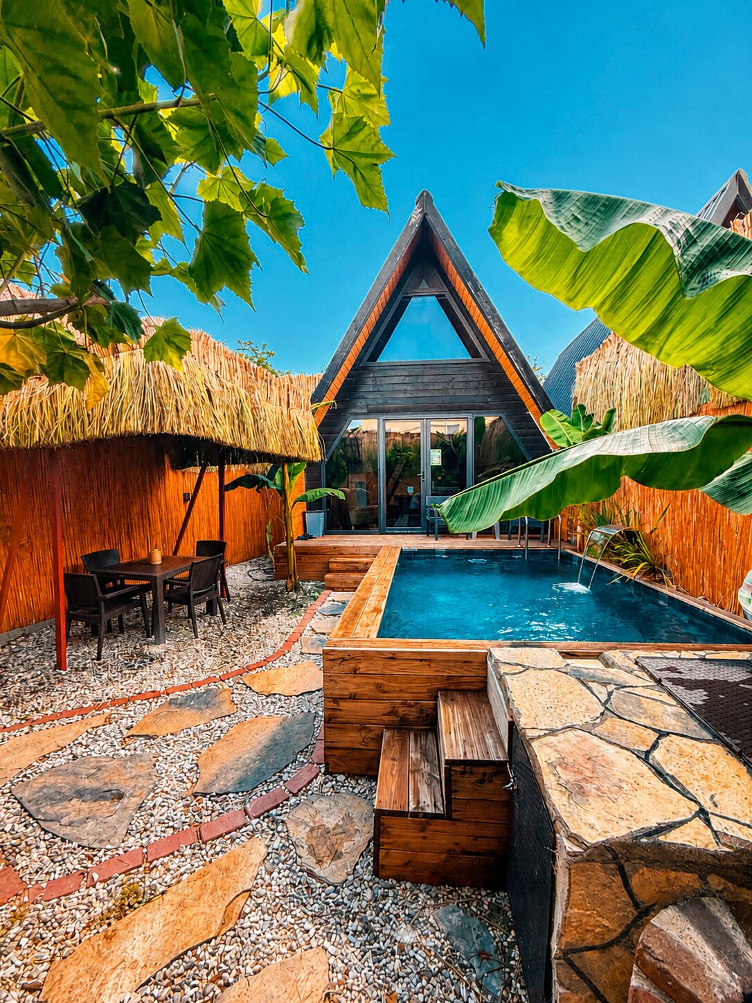 A modern villa with a swimming pool, wooden deck, and tropical vegetation.