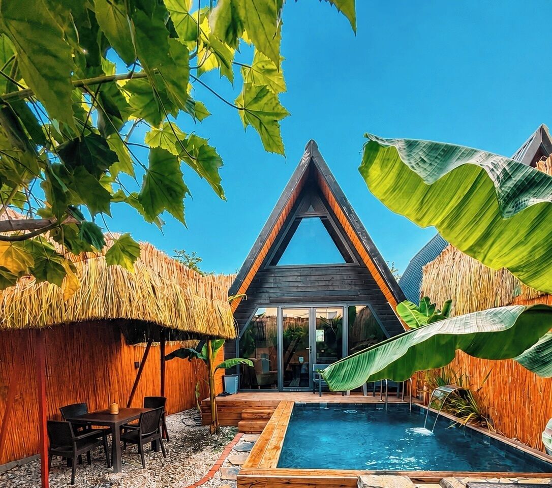 Una villa moderna con piscina, rodeada de vegetación tropical y construcciones con techo de paja.