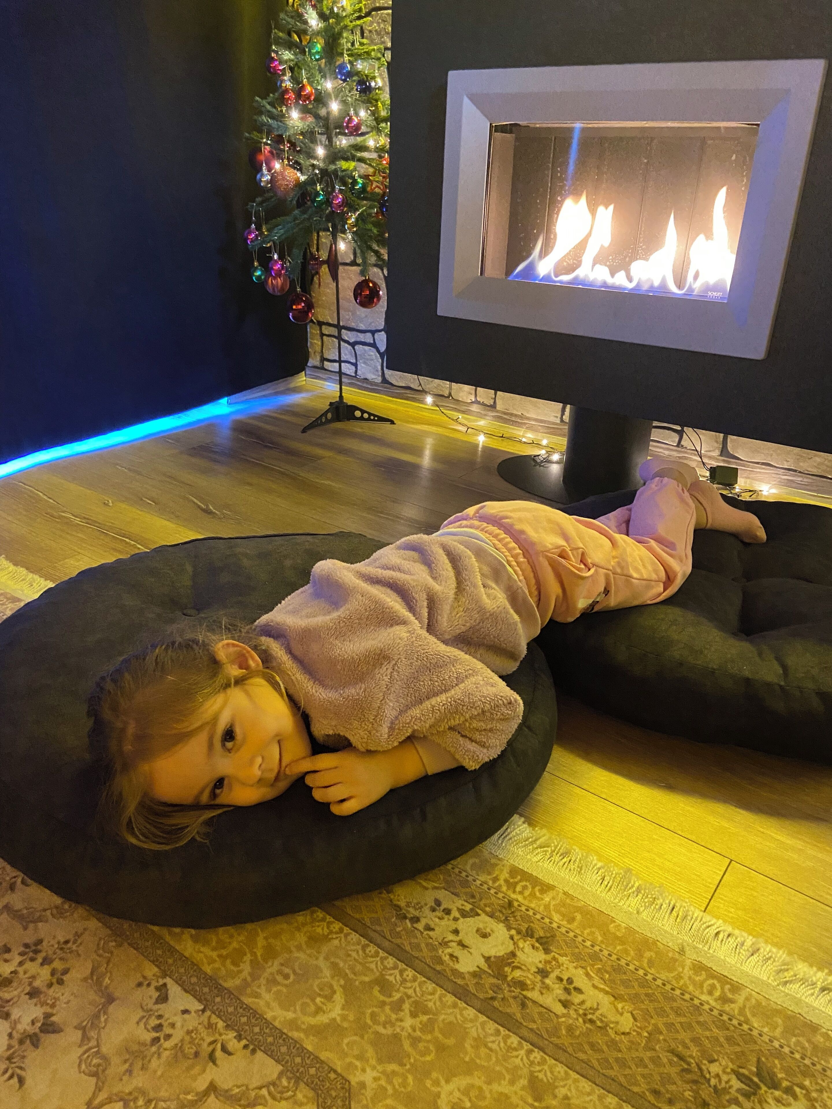 Un niño recostado sobre un sillón de tina negro en una habitación con chimenea, un árbol de Navidad y una alfombra estampada.