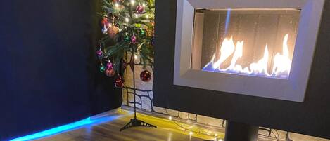 Un niño recostado sobre un sillón de tina negro en una habitación con chimenea, un árbol de Navidad y una alfombra estampada.
